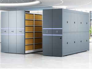 Two dark grey industrial mobile shelving units with dual-control system featuring front electric control panel and rear manual hand wheel backup, designed for high-density archive and library storage with six-tier adjustable shelf configuration.